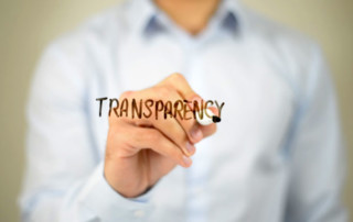 Image of a person drawing the word Transparency on a transparent board